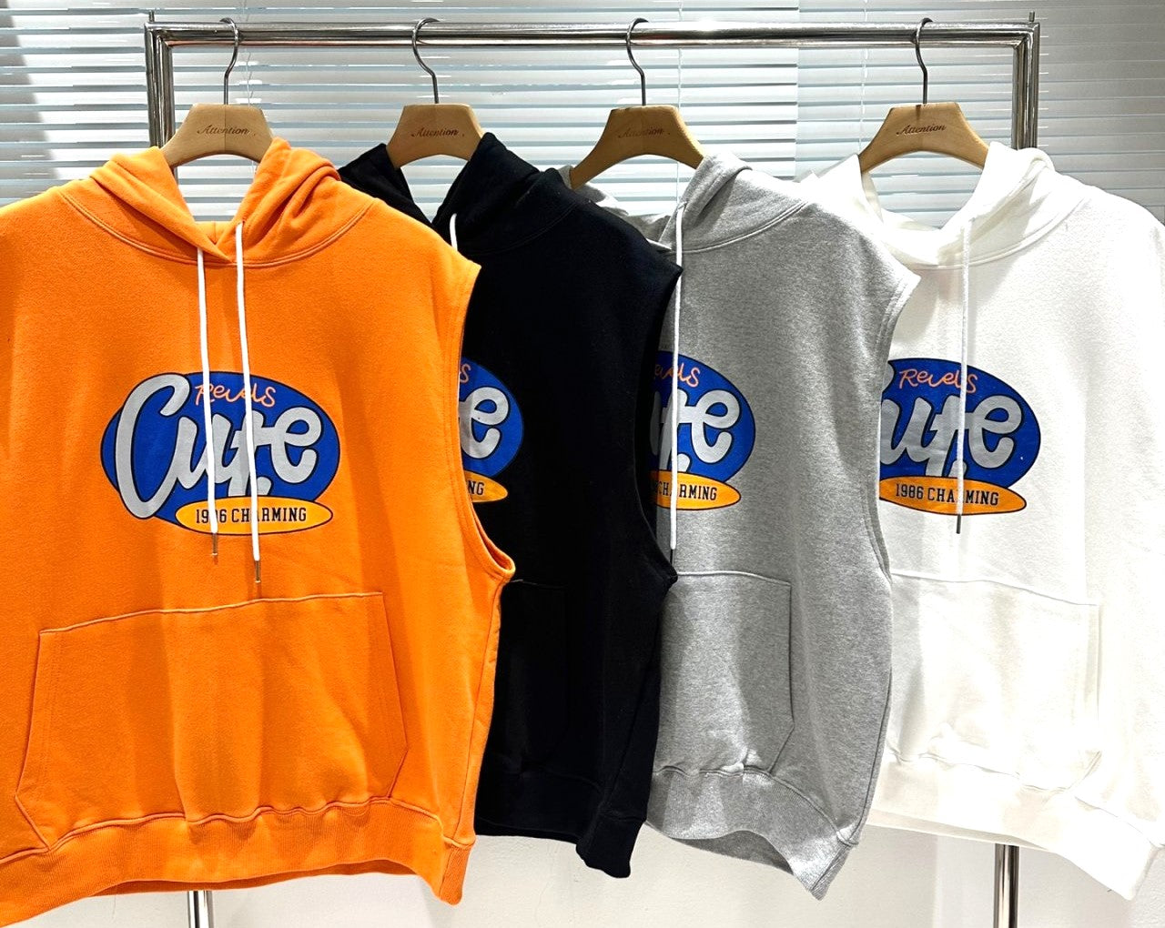 Orange Black Gray White sleeveless hoodie sweaters hanging on a rack. 