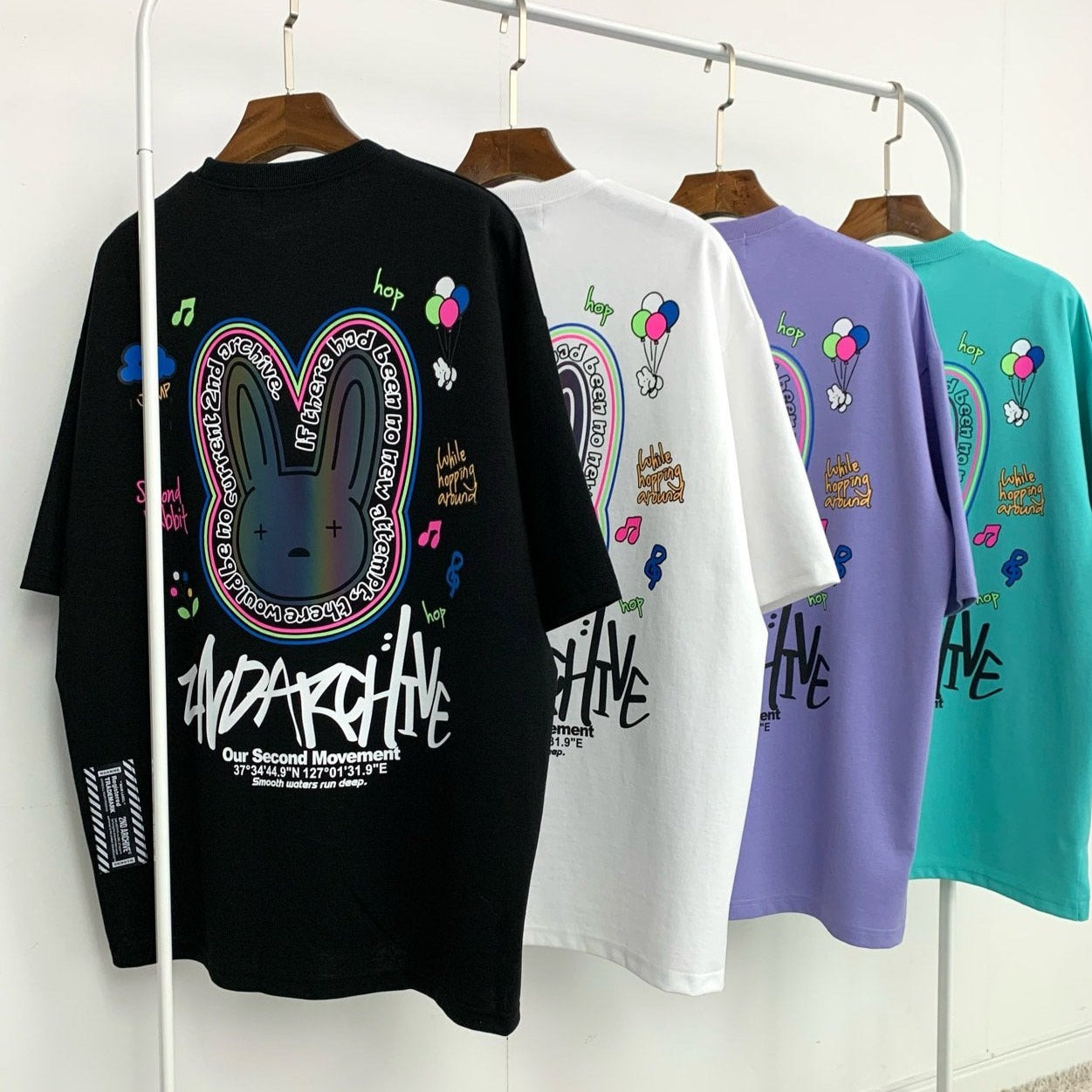 four different colored Korean street fashion graphic t's hanging on a rack. 