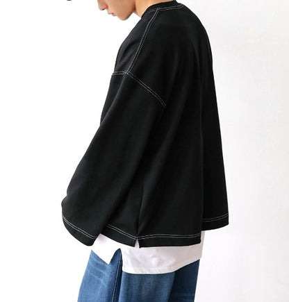 Side view of model wearing oversized unisex long sleeve black shirt with double stitching. 