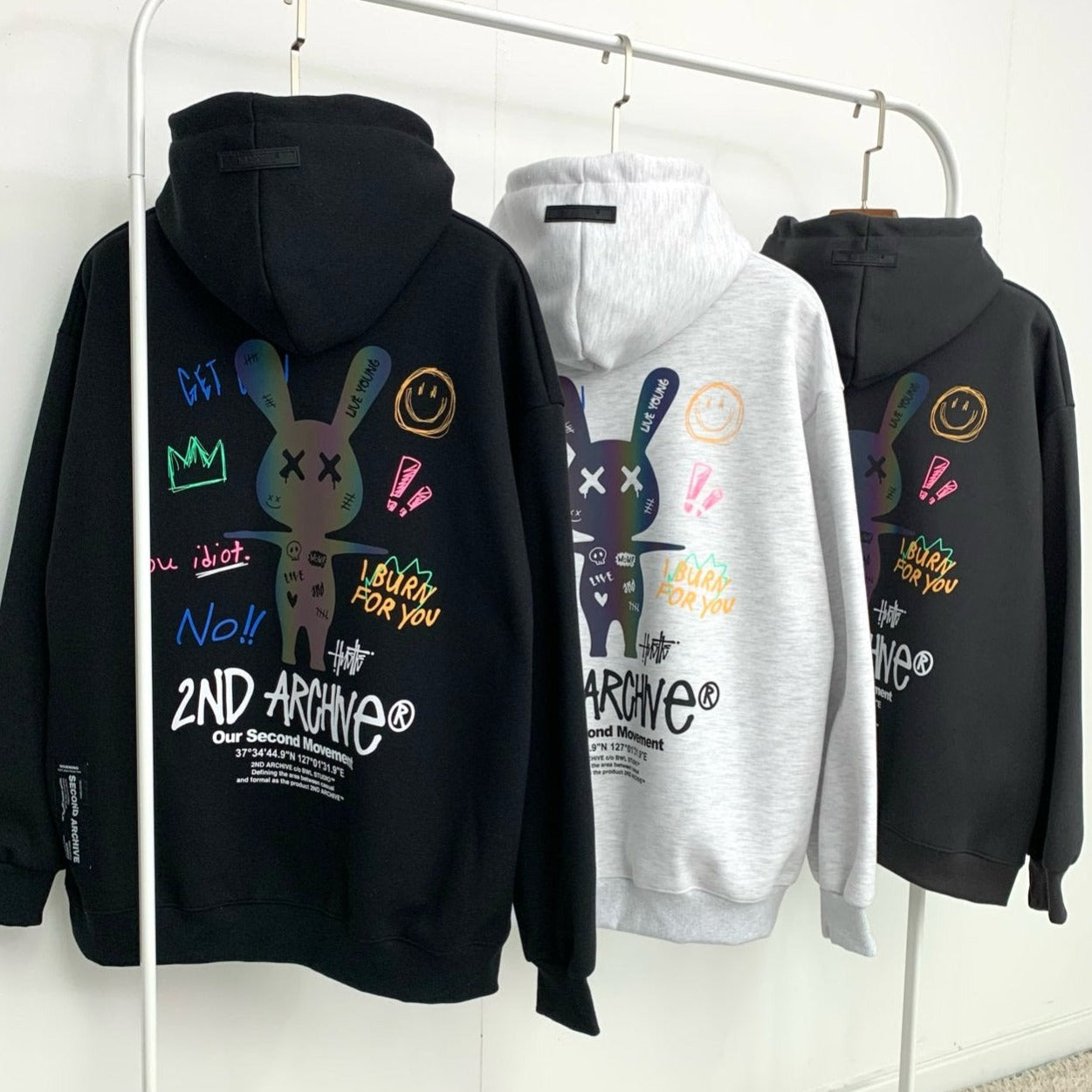 Back facing black, light gray and dark gray hoodie sweaters with street fashion graphics. 